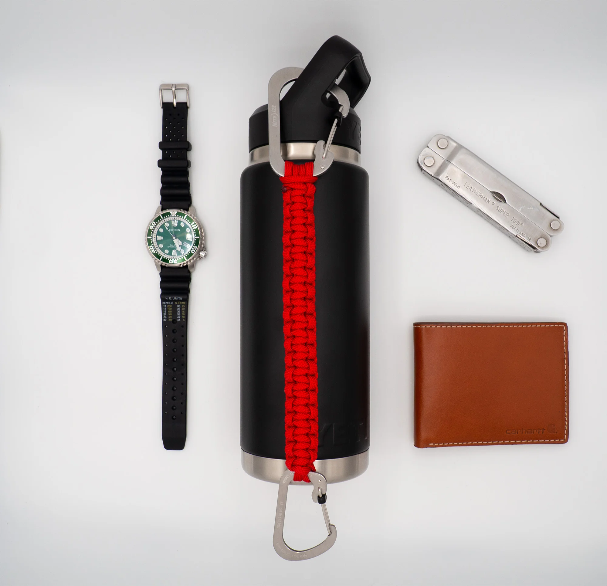 Red THIRSTLOCK™ ANCHOR™ bottle leash shown with everyday carry items including a watch, wallet, and multi-tool.